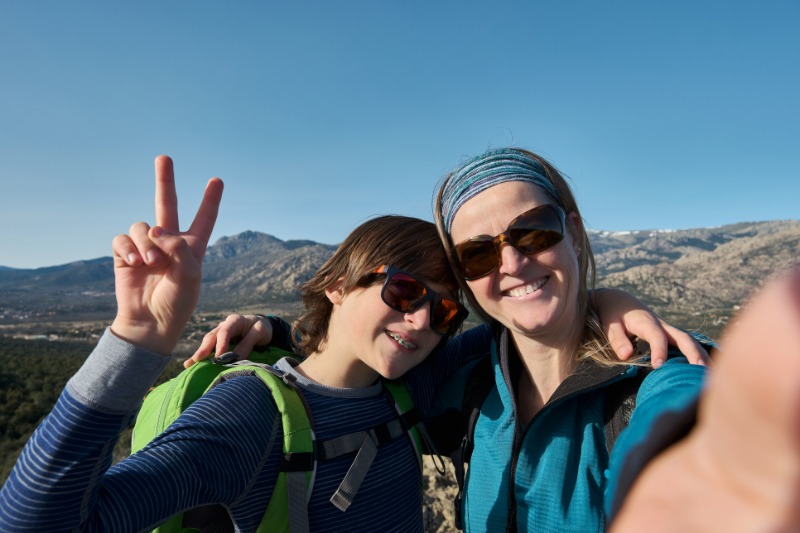 Teenage boy with braces and mother taking selfie during hiking in nature